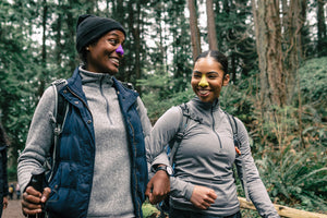 Two women hiking, smiling and wearing Noz sunscreen on their nose.